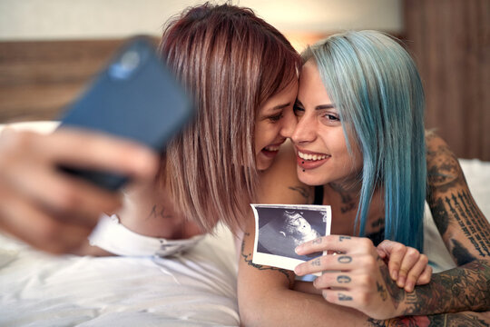 A young happy lesbian couple taking a selfie with ultrasound photo showing their baby. Love, pregnancy, lgbt, relationship