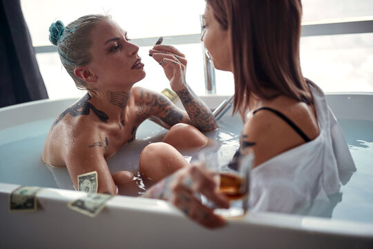 A young sexy tattooed lesbian couple in foreplay while enjoying moments of hedonism and luxury in a bath in the bathroom. Love, relationship, luxury, bath, lgbt