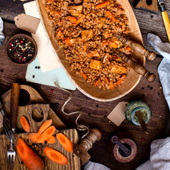 buckwheat porridge with meat and vegetables in wooden oval bowl on rustic table