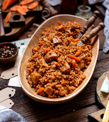 buckwheat porridge with meat and vegetables in wooden oval bowl on rustic table