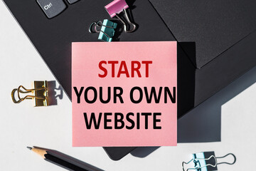 START YOUR OWN WEBSITE note is written on a paper sticker on a laptop keyboard.