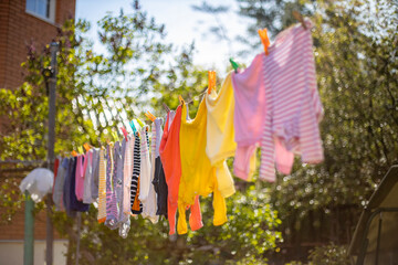 Baby cute clothes hanging on the clothesline outdoor. Child laundry hanging on line in garden on green background. Baby accessories.