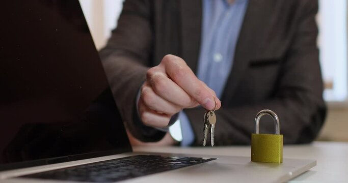 Close-up, a man brings the keys to the lock with his hand, the closed lock is on the case of an open laptop. The laptop is under reliable protection when the user has the keys.