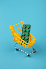 Shopping cart loaded with pills drugs or medicine on yellow background.antibiotics. Women's health, medicine and healthcare concept. Top view, copy space for text.