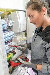 Woman electrician tests circuit breakers in a electrical panel