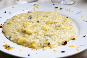 Risotto all’onda servito nel piatto di ceramica guarnito con petali di fiori commestibili