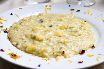 Risotto all’onda servito nel piatto di ceramica guarnito con petali di fiori commestibili