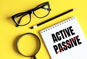 New PASSIVE - ACTIVE text written on a notebook with glasses, magnifying glass and pencil.