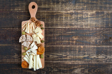 Different kinds of cheeses, dried apricots, whole-grain breads, nuts, olives, capers on a wooden board. Cheese board, snacks. Copy space. The top view