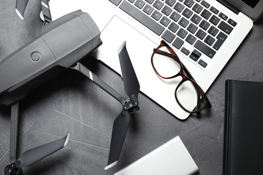 Modern drone with video camera and laptop on grey stone table, flat lay