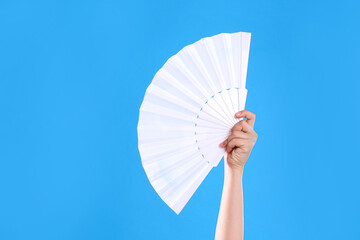 Woman holding white hand fan on light blue background, closeup - obrazy, fototapety, plakaty