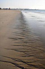 Vue sur une longue plage déserte avec des dessins en croisillons creusés par les mouvements de l'eau sur le sable jusqu'à l'horizon.