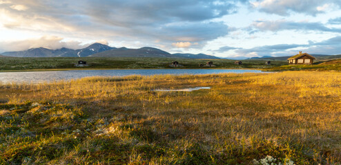 Fototapeta na wymiar Golden hour in mountain scenery with cabins and lake and dramatic skies.