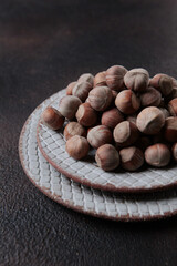 Hazelnuts in a ceramic plate on a dark background. Vertical photo. With copy space