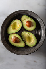 Fresh avocados in old metal bowl on marble background.