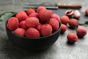 Fresh ripe lychee fruits in black ceramic bowl on grey table