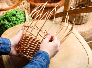 Fototapeta na wymiar Woman weaving wicker basket indoors, closeup view