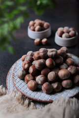 Hazelnuts in a ceramic plate . Lots of nuts on a dark background. Food with a high content of protein concentrate. Natural protein food. Linen napkin. Green branch is out of focus.