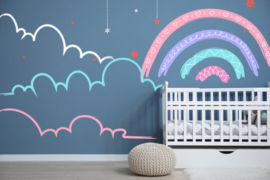 Interior of modern baby room with crib and painting of rainbow on wall