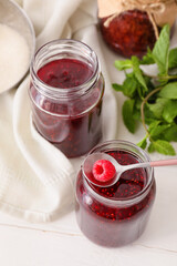 Glass jars with sweet raspberry jam on light background