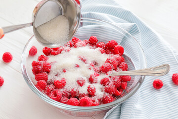 Adding sugar into bowl with ripe raspberry on wooden background