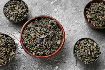 Bowls with dry tea leaves on grunge background