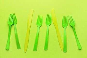 Plastic forks and knives on color background