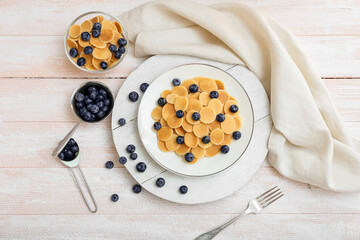 Plates of tasty pancakes with fresh blueberry on light wooden background