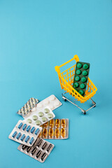 Shopping cart loaded with pills on blue background. The concept of medicine and the sale of drugs. Copy space.