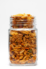 Pile of Indian spicy snacks (Namkeen) - (All in one) in a glass jar, made with fried peanut, corn flakes, sweet pea, pulses, cashew nuts. Front view, against the white background.