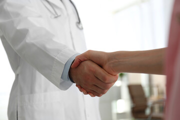 Fototapeta premium Doctor and patient shaking hands in clinic, closeup