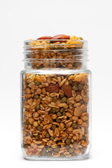 Shahi Mixture in a glass jar, made with peanut, cashew, corn flakes, almonds, etc. Pile of Indian spicy snacks (Namkeen). front view, against the white background