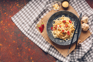 Plate with tasty noodles, chicken and chopsticks on grunge background