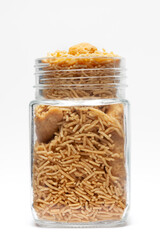 Indian spicy snacks (Namkeen) - Bikaneri Besan Bhujia in a glass jar, made with chickpea flour (Besan), Front view, against the white background.