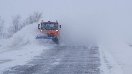 Winter. Heavy snowfall, blizzard. A special car clears the road of snow. Part of the image is blurred.
