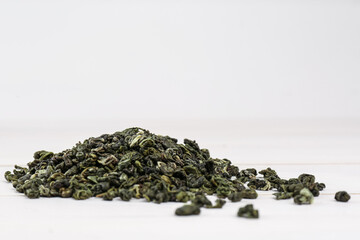 Heap of dried green tea leaves on white table