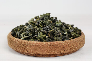 Fototapeta na wymiar Dried green tea leaves in cork bowl on white table, closeup