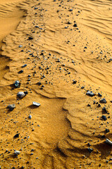 Gros Plan sur des petits cailloux gris posés à la surface du sable doré dans le désert.