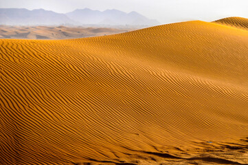 Vue sur une dune de sable doré dans le désert avec des montagnes en arrière-plan.