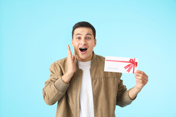 Surprised young man with gift card on color background