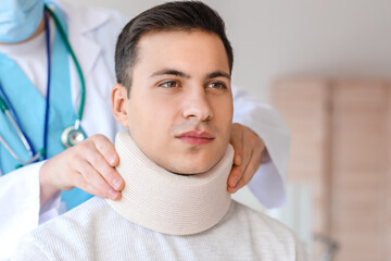Doctor applying cervical collar on neck of young man in clinic
