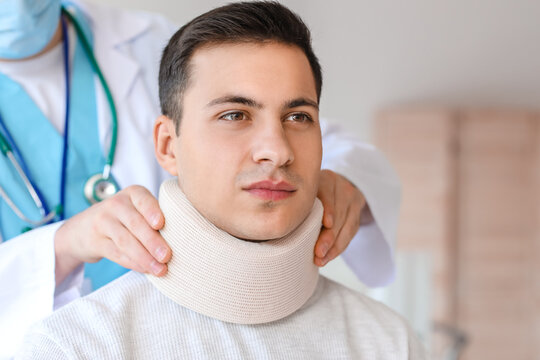 Doctor applying cervical collar on neck of young man in clinic - Powered by Adobe