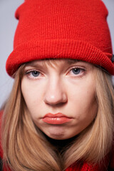Young blonde girl in red beanie expressing sadness or disappointment emotion. Pretty female model in red beanie hat and scarf looking straight in camera