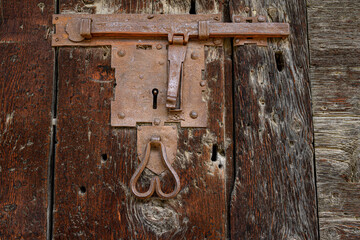 Primo piano di un’antica serratura a chiave, chiavistello e battente arrugginiti su un antico portone di un castello