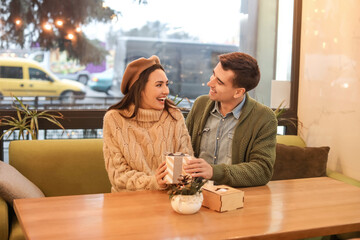 Happy young couple with Christmas gift in cafe