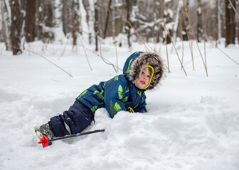 Fototapeta na wymiar A boy plays lying in a snowdrift in a winter forest