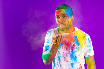 Afro american man celebrate holi festival in violet studio background