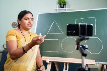 Indian woman explaining to students from board during online class in front of mobile phone - Concept of e-teaching, Remote learning, virtual education during covid-19 pandemic