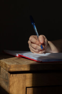 Mano de ni&ntilde;o escribe con birome sobre cuaderno mientras le da el sol