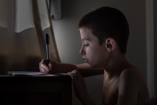 Ni&ntilde;o de pelo corto escribe en su cuaderno con iluminaci&oacute;n natural